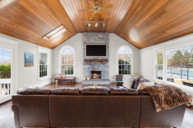 living room with a ceiling fan, a fireplace, rail lighting, wood ceiling, and lofted ceiling with skylight