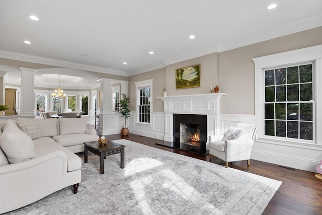 living area featuring a notable chandelier, a decorative wall, ornate columns, and dark wood-style floors