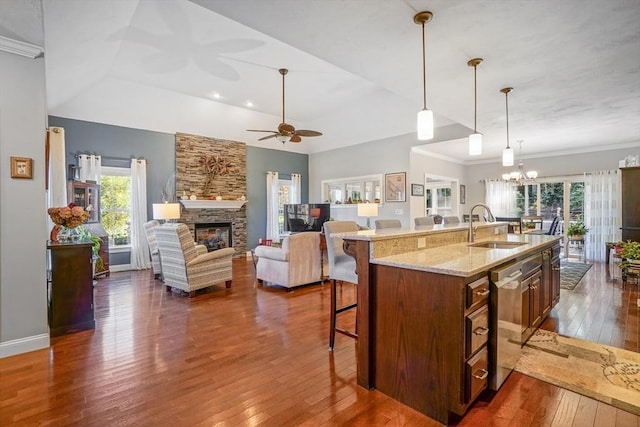 kitchen with a kitchen breakfast bar, a stone fireplace, dishwasher, a sink, and dark wood-style floors