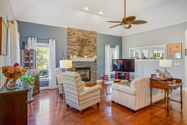 living room with baseboards, a stone fireplace, a ceiling fan, and wood finished floors