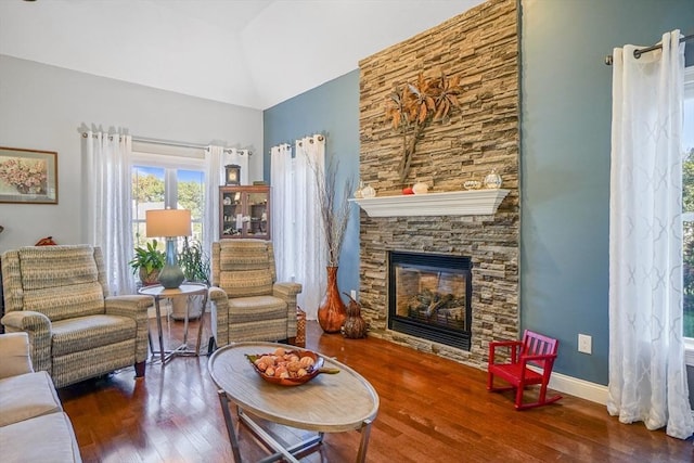 living room with high vaulted ceiling, baseboards, a stone fireplace, and wood finished floors