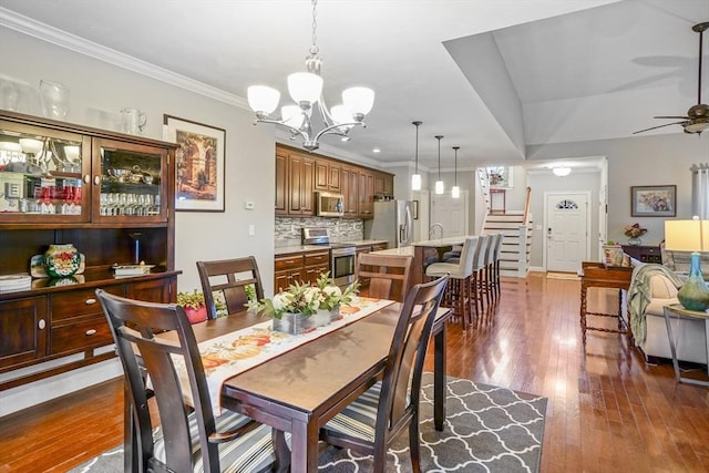 dining space featuring ornamental molding, stairs, hardwood / wood-style floors, baseboards, and ceiling fan with notable chandelier