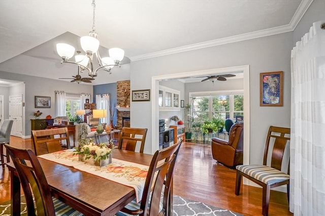 dining area with ornamental molding, ceiling fan with notable chandelier, wood finished floors, and a fireplace