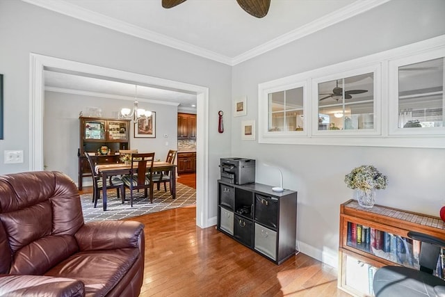 living area featuring crown molding, baseboards, ceiling fan with notable chandelier, and wood finished floors