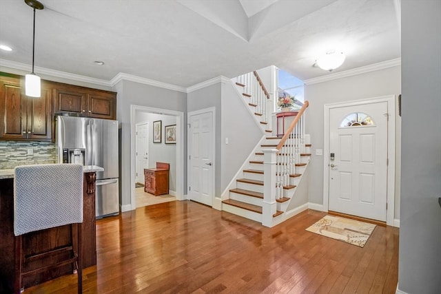foyer entrance with crown molding, baseboards, stairs, and wood finished floors