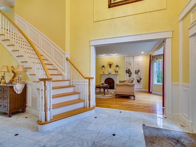 14 Nassau Dr, Winchester, MA 01890 - staircase featuring crown molding, a decorative wall, a fireplace, visible vents, and a high ceiling