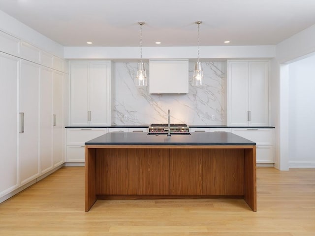 kitchen featuring pendant lighting, a kitchen island with sink, white cabinets, sink, and light hardwood / wood-style floors