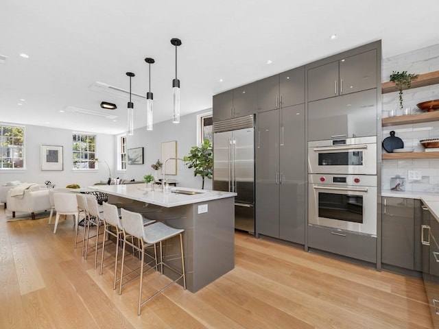 kitchen featuring tasteful backsplash, stainless steel appliances, pendant lighting, sink, and light hardwood / wood-style floors