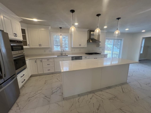 kitchen featuring wall chimney exhaust hood, sink, decorative light fixtures, a center island, and stainless steel appliances