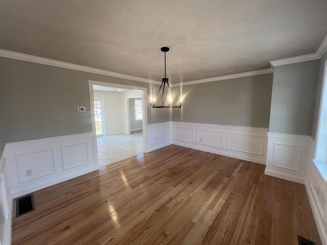 unfurnished dining area with hardwood / wood-style flooring, ornamental molding, and an inviting chandelier