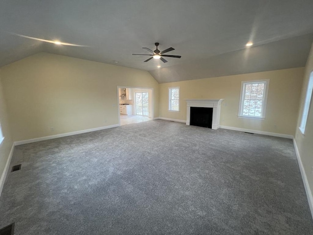 unfurnished living room featuring ceiling fan, a healthy amount of sunlight, lofted ceiling, and dark carpet