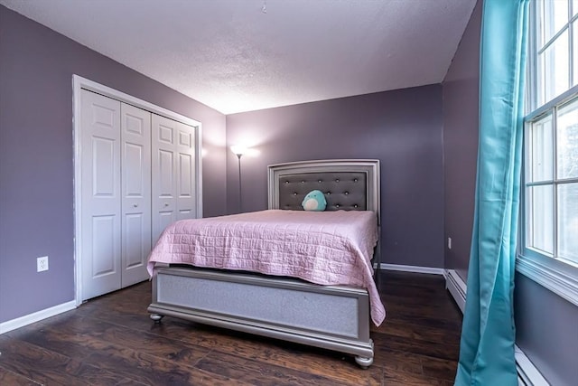 bedroom with a baseboard heating unit, a closet, and dark wood-type flooring