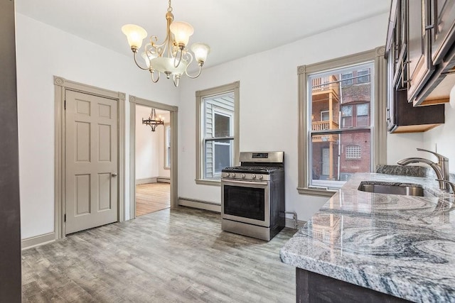 kitchen featuring gas range, baseboard heating, light wood-style floors, a notable chandelier, and a sink