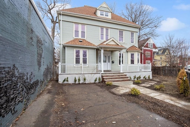 view of front of property featuring driveway, fence, covered porch, and roof with shingles