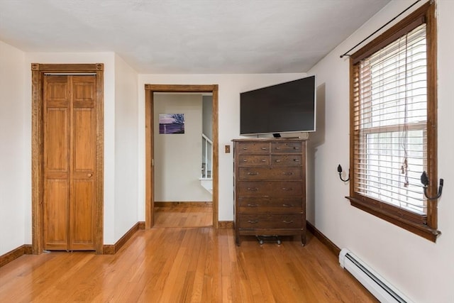 unfurnished bedroom featuring light wood finished floors, baseboards, and a baseboard radiator