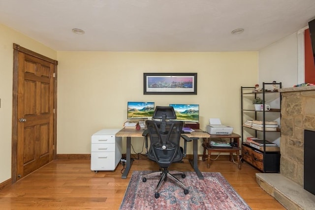 office space featuring baseboards, light wood-style floors, and a fireplace