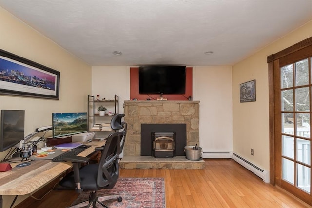 office with a baseboard heating unit, hardwood / wood-style flooring, and a wood stove