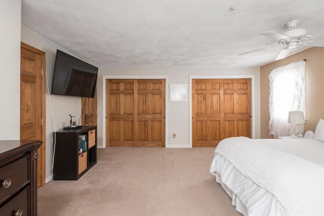 bedroom with a ceiling fan, baseboards, two closets, and light carpet