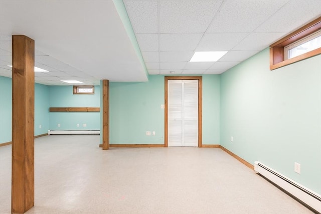 basement featuring a baseboard heating unit, baseboards, a drop ceiling, tile patterned floors, and a baseboard radiator