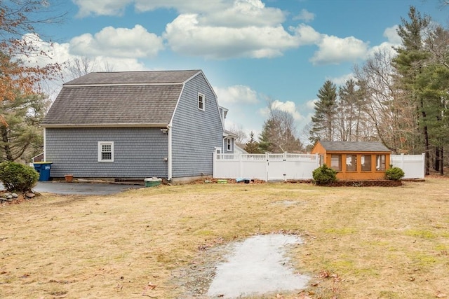 view of property exterior with an outbuilding, fence, a yard, a gambrel roof, and a shingled roof