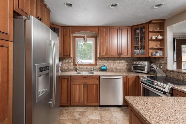 kitchen featuring a sink, decorative backsplash, brown cabinets, stainless steel appliances, and open shelves