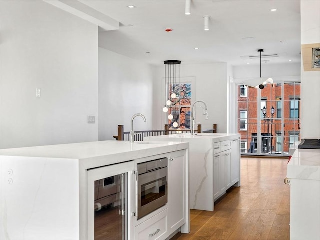 kitchen with white cabinets, wine cooler, a center island with sink, and decorative light fixtures