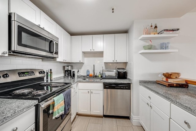 kitchen featuring light stone countertops, a sink, backsplash, white cabinets, and appliances with stainless steel finishes