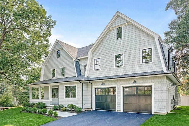 shingle-style home with an attached garage, a front yard, aphalt driveway, and a gambrel roof