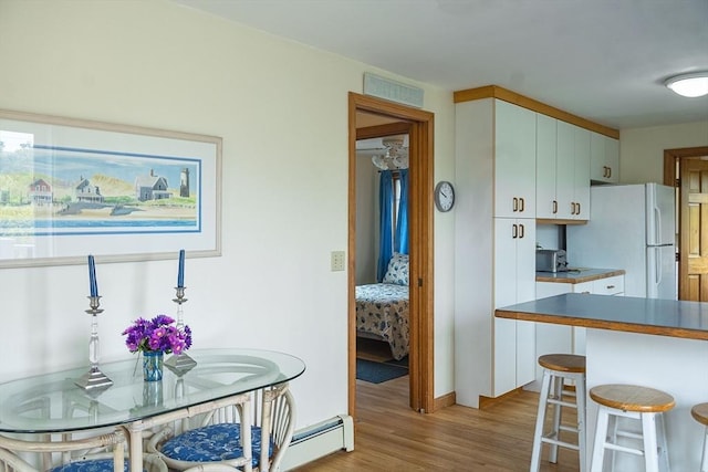 99 N Shore Blvd Unit 1, Sandwich, MA 02537 - kitchen with freestanding refrigerator, light wood-style floors, a baseboard heating unit, a kitchen breakfast bar, and white cabinetry