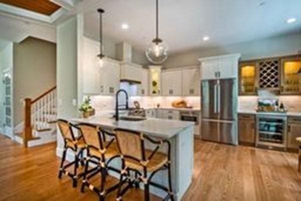 kitchen featuring hanging light fixtures, stainless steel fridge, light wood-type flooring, white cabinetry, and beverage cooler