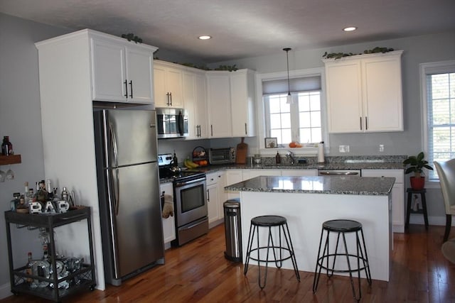 kitchen featuring a center island, hanging light fixtures, dark stone counters, stainless steel appliances, and white cabinets