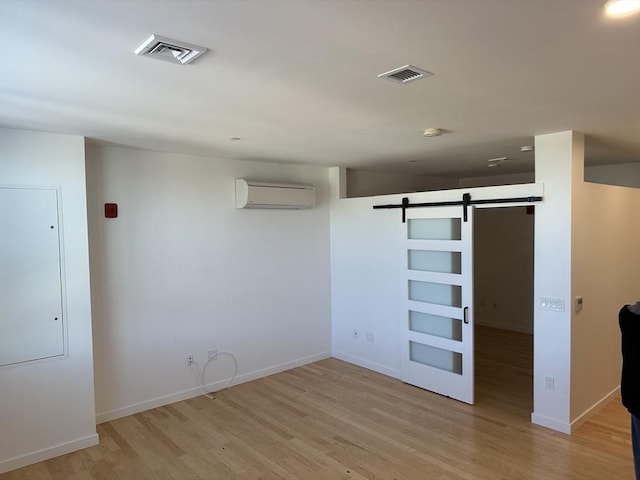 spare room featuring a barn door, a wall unit AC, and light hardwood / wood-style flooring