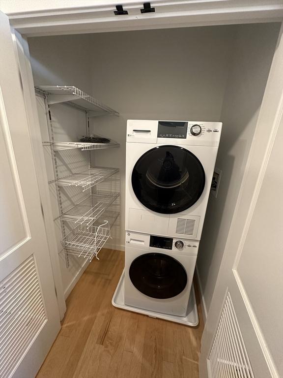 laundry room featuring stacked washing maching and dryer and hardwood / wood-style flooring