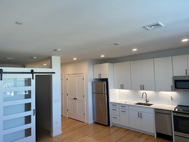 kitchen featuring white cabinets, sink, light hardwood / wood-style flooring, a barn door, and stainless steel appliances