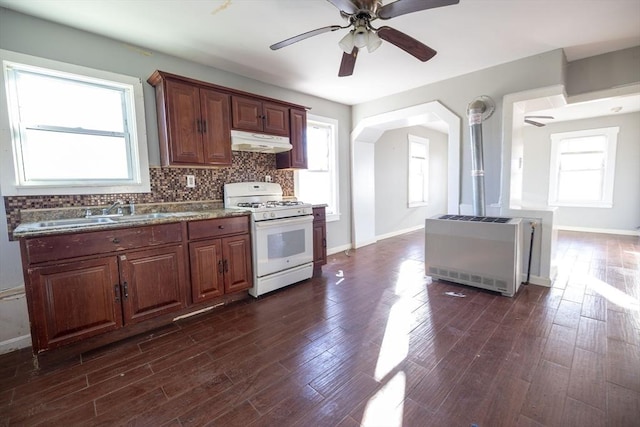 kitchen with white gas range oven, decorative backsplash, ceiling fan, dark hardwood / wood-style flooring, and heating unit