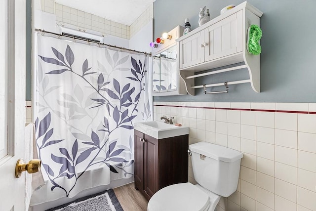 bathroom with toilet, vanity, wainscoting, shower / tub combo, and tile walls