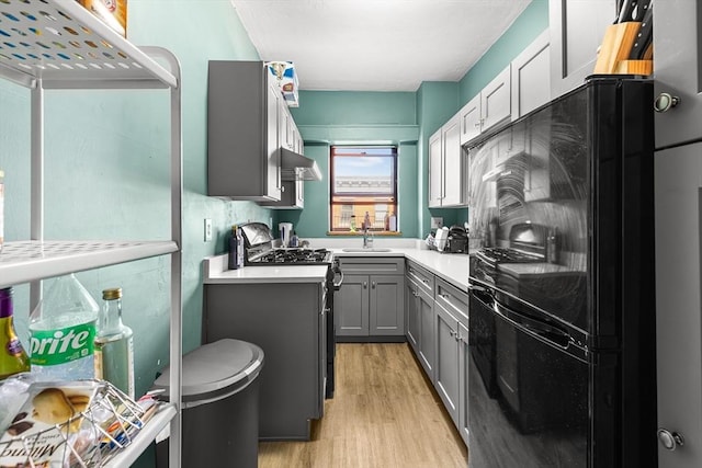 kitchen with gray cabinets, freestanding refrigerator, gas stove, light wood-style floors, and light countertops