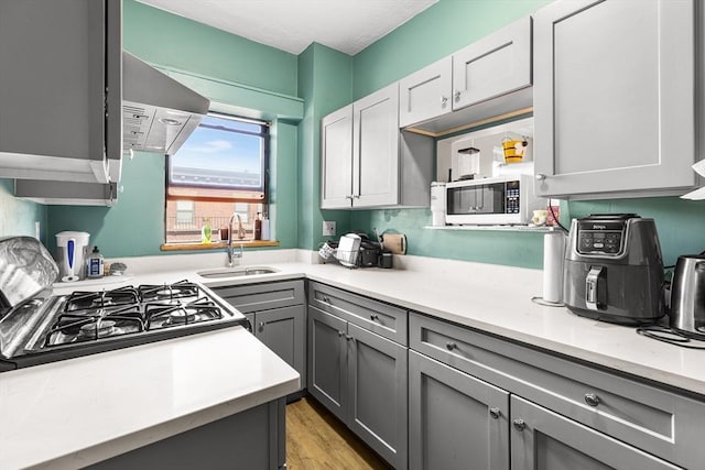 kitchen with a sink, light countertops, gray cabinets, and black gas stove