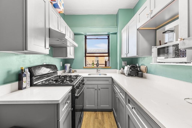 kitchen featuring gray cabinets, under cabinet range hood, a sink, white microwave, and black range with gas stovetop