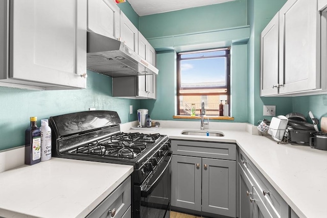 kitchen with black gas stove, gray cabinetry, under cabinet range hood, light countertops, and a sink