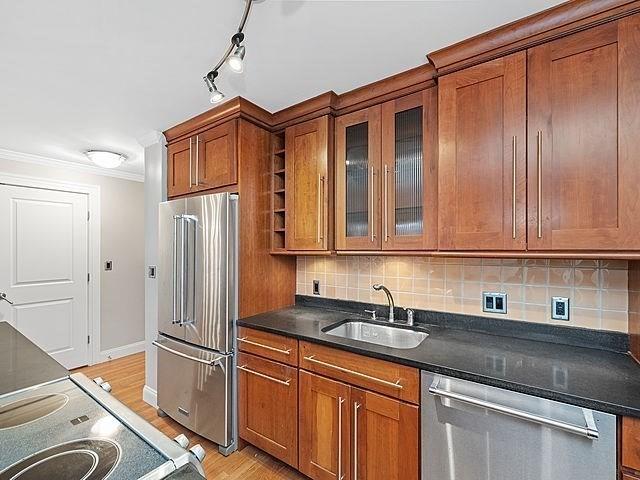 kitchen featuring dark countertops, backsplash, brown cabinets, appliances with stainless steel finishes, and a sink