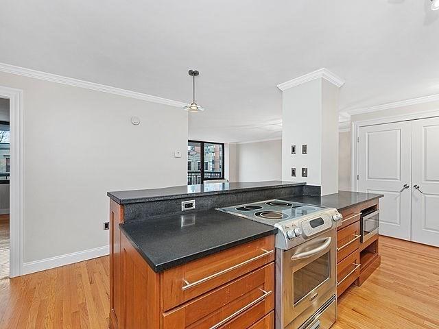 kitchen featuring brown cabinets, dark countertops, stainless steel appliances, crown molding, and light wood finished floors