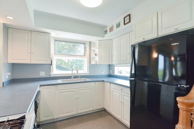 kitchen with white cabinets, sink, range, and black fridge