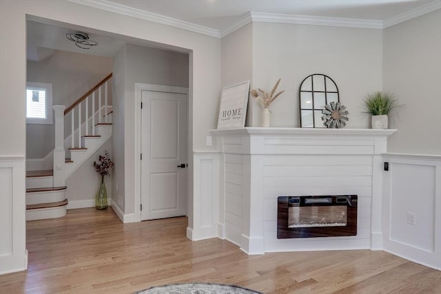 living area featuring ornamental molding, a glass covered fireplace, light wood-style floors, and stairs