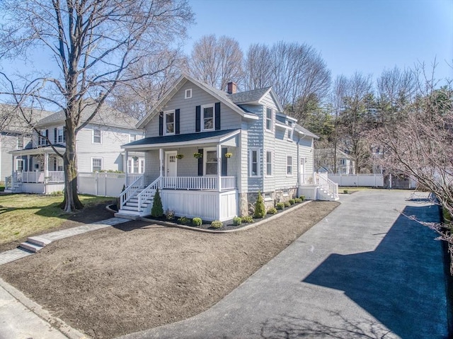 american foursquare style home with a porch, a chimney, aphalt driveway, and fence