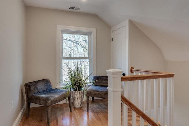 living area with an upstairs landing, visible vents, vaulted ceiling, and wood finished floors