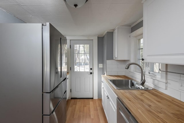 kitchen with tasteful backsplash, white cabinets, light wood-style flooring, appliances with stainless steel finishes, and a sink