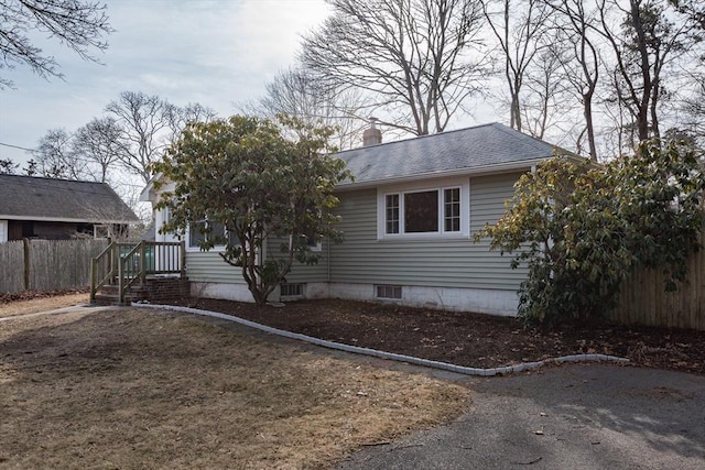 view of front of home with a shingled roof, a chimney, and fence