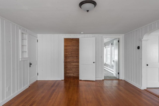 unfurnished bedroom featuring arched walkways, dark wood finished floors, and baseboard heating