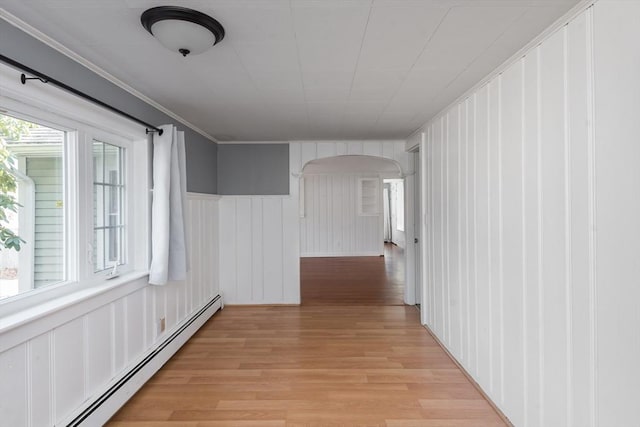 hallway with arched walkways, ornamental molding, baseboard heating, and light wood-style floors